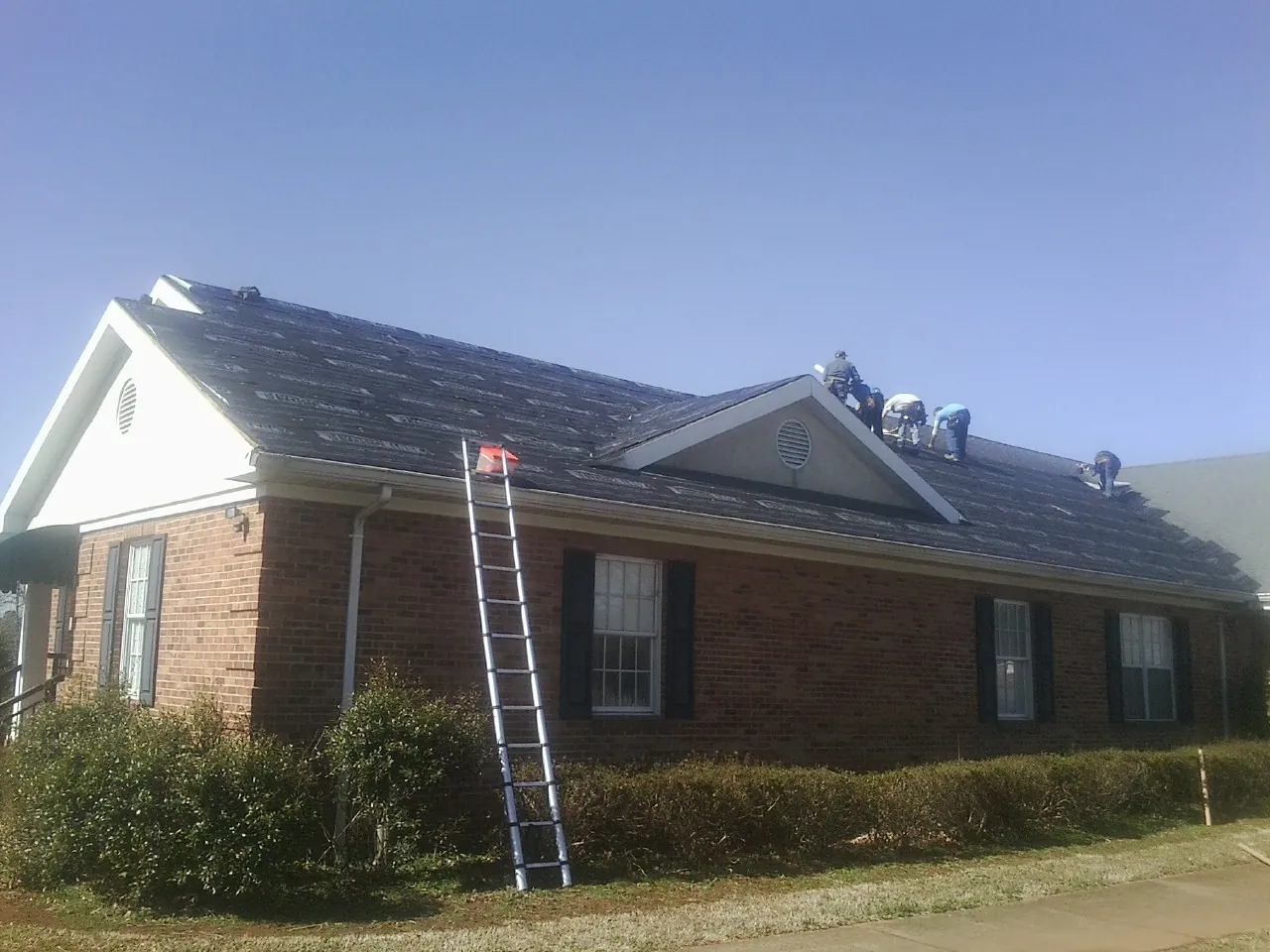 Crew tearing shingles off a brick ranch roof with a ladder set — Emergency Roof Repair work by our crew in Redding